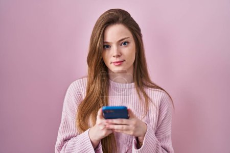 Photo for Young caucasian woman using smartphone typing message relaxed with serious expression on face. simple and natural looking at the camera. - Royalty Free Image