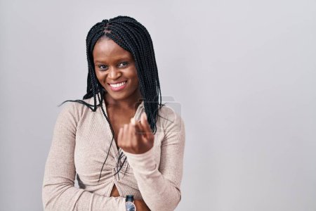 Foto de Mujer africana con trenzas de pie sobre fondo blanco haciendo señas ven aquí gesto con la mano invitando a la bienvenida feliz y sonriente - Imagen libre de derechos