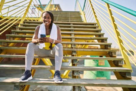 Téléchargez les photos : Femme afro-américaine en utilisant smartphone assis sur les escaliers à la rue - en image libre de droit