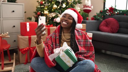 Photo for African woman taking selfie picture with christmas present at home - Royalty Free Image