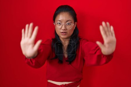 Téléchargez les photos : Asiatique jeune femme debout sur fond rouge faire arrêter geste avec les mains paumes, expression de colère et de frustration - en image libre de droit