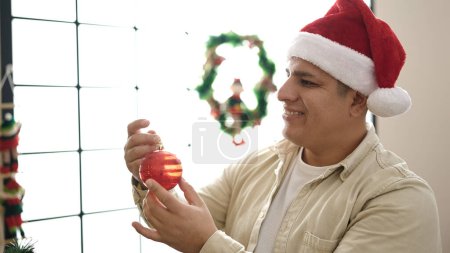 Foto de Joven hombre hispano decorando árbol de navidad en casa - Imagen libre de derechos