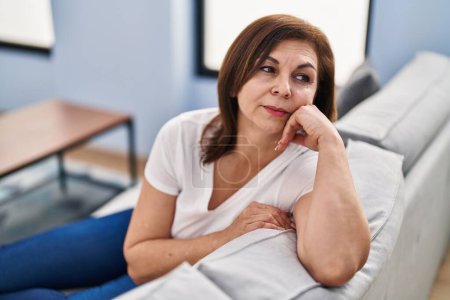 Photo for Middle age woman sitting on sofa with serious expression at home - Royalty Free Image