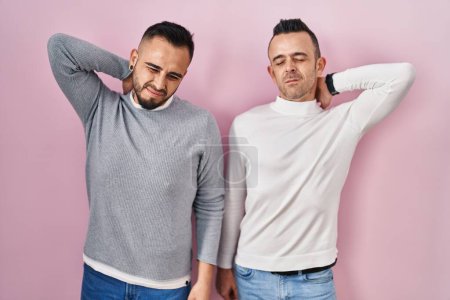Photo for Homosexual couple standing over pink background suffering of neck ache injury, touching neck with hand, muscular pain - Royalty Free Image