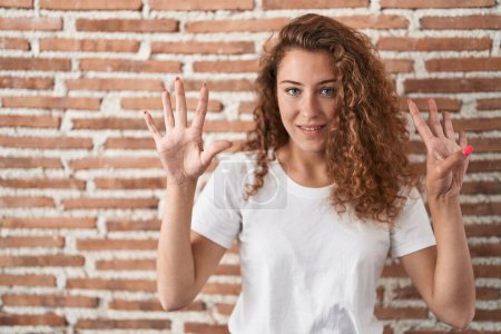 Téléchargez les photos : Jeune femme caucasienne debout sur le fond de mur de briques montrant et pointant vers le haut avec les doigts numéro neuf tout en souriant confiant et heureux. - en image libre de droit