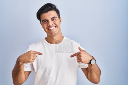 Photo for Hispanic man standing over blue background looking confident with smile on face, pointing oneself with fingers proud and happy. - Royalty Free Image