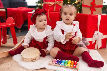 Foto de Adorables chicas jugando xilófono y pandereta celebrando la Navidad en casa - Imagen libre de derechos