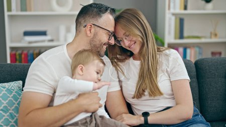 Téléchargez les photos : Famille de mère, père et bébé souriant assis sur le canapé à la maison - en image libre de droit