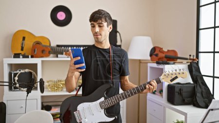 Téléchargez les photos : Jeune guitariste hispanique, composer les électro-airs, textos tout en s'attaquant à la guitare électrique dans le studio de musique - en image libre de droit