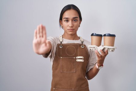 Photo for Young hispanic woman wearing professional waitress apron holding coffee doing stop sing with palm of the hand. warning expression with negative and serious gesture on the face. - Royalty Free Image
