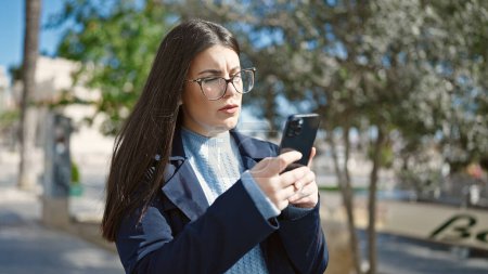 Téléchargez les photos : Jeune femme hispanique utilisant smartphone regardant bouleversé au parc - en image libre de droit