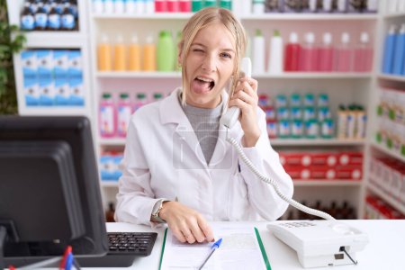 Photo for Young caucasian woman working at pharmacy drugstore speaking on the telephone sticking tongue out happy with funny expression. emotion concept. - Royalty Free Image