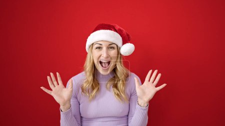 Foto de Mujer hispana hermosa joven expresión sorpresa usando sombrero de Navidad sobre fondo rojo aislado - Imagen libre de derechos