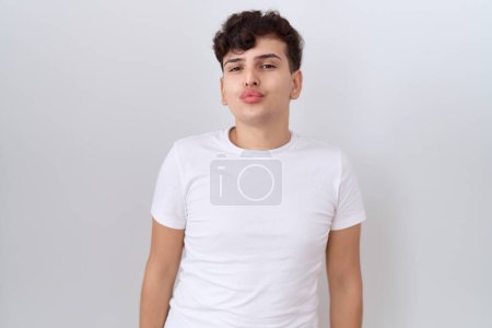 Téléchargez les photos : Jeune homme non binaire portant t-shirt blanc décontracté regardant la caméra souffler un baiser sur l'air étant belle et sexy. expression d'amour. - en image libre de droit