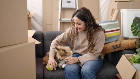 Téléchargez les photos : Jeune femme hispanique avec chien assis sur le canapé jouant avec la balle à la nouvelle maison - en image libre de droit