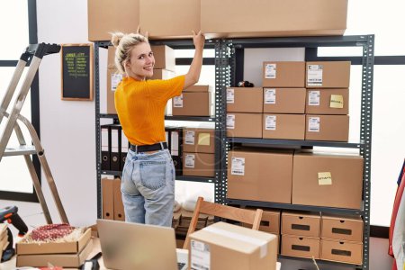 Photo for Young blonde woman ecommerce business worker organizing packages on shelving at office - Royalty Free Image