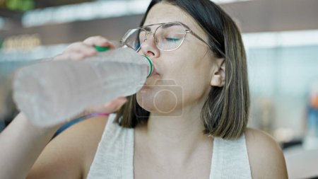 Foto de Joven mujer hispana hermosa bebiendo botella de agua en el aeropuerto - Imagen libre de derechos
