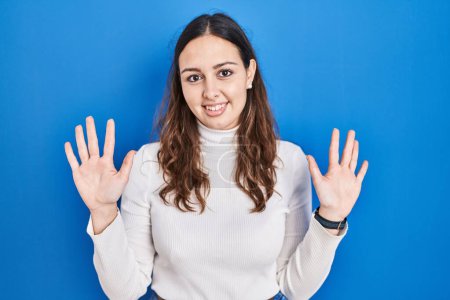 Téléchargez les photos : Jeune femme hispanique debout sur fond bleu montrant et pointant vers le haut avec les doigts numéro dix tout en souriant confiant et heureux. - en image libre de droit