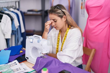 Foto de Young blonde woman tailor stressed using sewing machine at clothing shop - Imagen libre de derechos