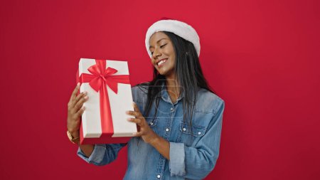 Foto de Mujer afroamericana sosteniendo regalo de Navidad sobre fondo rojo aislado - Imagen libre de derechos
