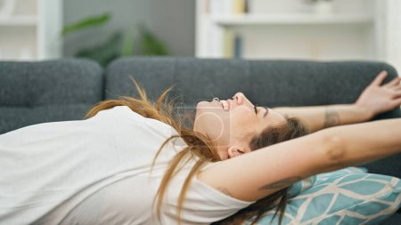 Téléchargez les photos : Jeune belle femme hispanique allongée sur un canapé étirant les bras à la maison - en image libre de droit
