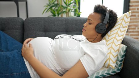 Photo for Young pregnant woman listening to music sleeping on sofa at home - Royalty Free Image