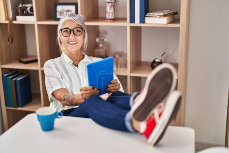 Photo for Middle age grey-haired woman drinking coffee and using touchpad at home - Royalty Free Image