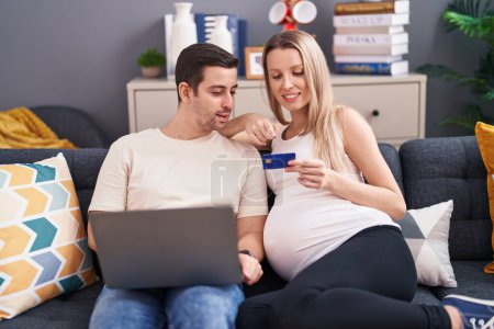 Foto de Hombre y mujer pareja usando portátil y tarjeta de crédito esperando bebé en casa - Imagen libre de derechos