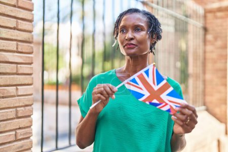 Téléchargez les photos : Moyen Age femme afro-américaine tenant drapeau du royaume uni dans la rue - en image libre de droit