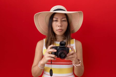 Téléchargez les photos : Femme chinoise du Moyen Age utilisant un appareil photo réflexe portant un chapeau d'été déprimé et inquiet pour la détresse, pleurer en colère et effrayé. triste expression. - en image libre de droit