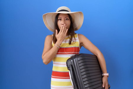 Téléchargez les photos : Femme chinoise du Moyen Age tenant une valise allant en vacances d'été couvrant la bouche avec la main, choquée et effrayée par l'erreur. expression surprise - en image libre de droit