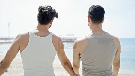 Téléchargez les photos : Deux hommes couple debout vers l'arrière avec les mains ensemble au bord de la mer - en image libre de droit