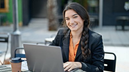 Foto de Joven hermosa mujer hispana trabajadora de negocios usando laptop sonriendo en la terraza de la cafetería - Imagen libre de derechos