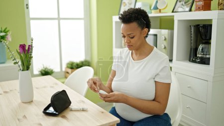 Foto de Mujer embarazada joven midiendo azúcar sentada en la mesa en el comedor - Imagen libre de derechos