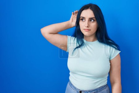 Photo for Young modern girl with blue hair standing over blue background smiling with hand over ear listening an hearing to rumor or gossip. deafness concept. - Royalty Free Image