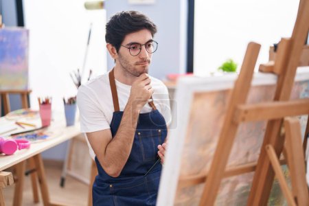 Foto de Young hispanic man artist looking draw with doubt expression at art studio - Imagen libre de derechos