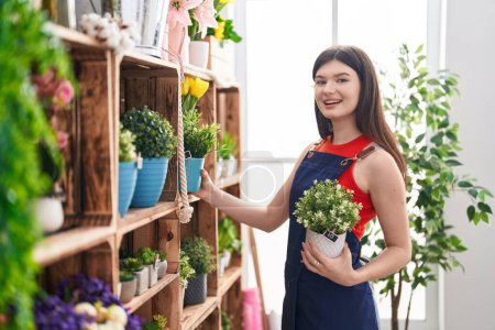 Téléchargez les photos : Jeune femme caucasienne fleuriste tenant plante chez le fleuriste - en image libre de droit
