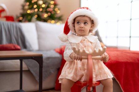 Photo for Adorable caucasian girl playing with reindeer rocking by christmas tree at home - Royalty Free Image