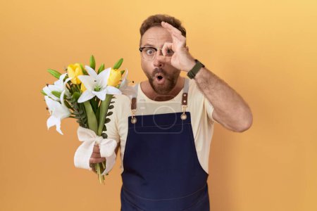 Téléchargez les photos : Homme du Moyen Age avec magasin de fleuriste barbe tenant des fleurs faisant geste ok choqué par le visage surpris, oeil regardant à travers les doigts. expression incrédule. - en image libre de droit