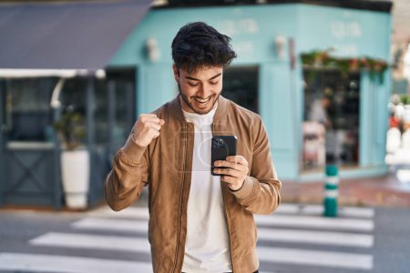 Foto de Joven hombre hispano sonriendo confiado usando smartphone en la calle - Imagen libre de derechos