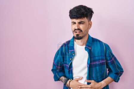Photo for Young hispanic man with beard standing over pink background with hand on stomach because indigestion, painful illness feeling unwell. ache concept. - Royalty Free Image