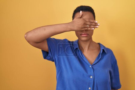 Photo for African american woman standing over yellow background covering eyes with hand, looking serious and sad. sightless, hiding and rejection concept - Royalty Free Image