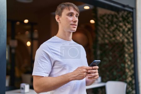 Téléchargez les photos : Jeune homme caucasien souriant confiant en utilisant smartphone à la terrasse du café - en image libre de droit