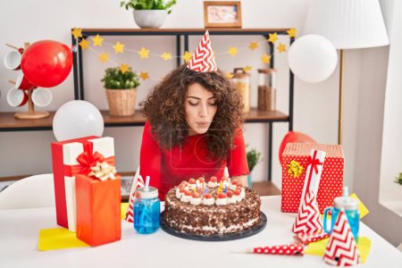 Photo for Young hispanic woman celebrating birthday blowing out candles at home - Royalty Free Image