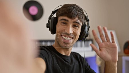 Foto de Guapo, joven músico hispano, se involucra apasionadamente en una conversación musical, cantando y hablando en una videollamada en un estudio de música de interior. - Imagen libre de derechos
