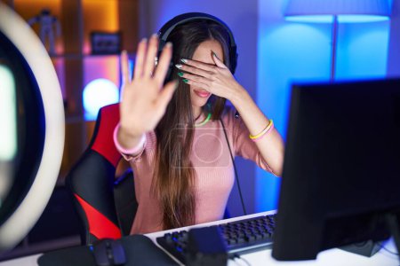 Photo for Young hispanic woman playing video games covering eyes with hands and doing stop gesture with sad and fear expression. embarrassed and negative concept. - Royalty Free Image