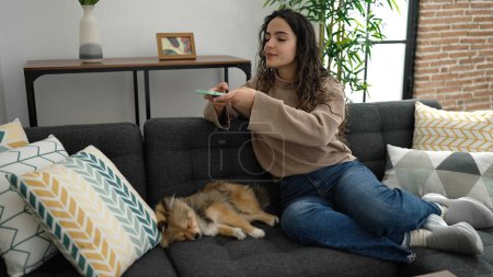 Foto de Joven mujer hispana con perro hacer foto por teléfono inteligente a perro dormido en casa - Imagen libre de derechos