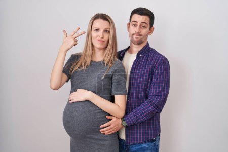 Photo for Young couple expecting a baby standing over white background shooting and killing oneself pointing hand and fingers to head like gun, suicide gesture. - Royalty Free Image