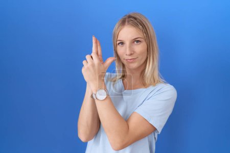 Foto de Mujer caucásica joven con camiseta azul casual sosteniendo arma simbólica con gesto de mano, jugando a matar armas de fuego, cara enojada - Imagen libre de derechos