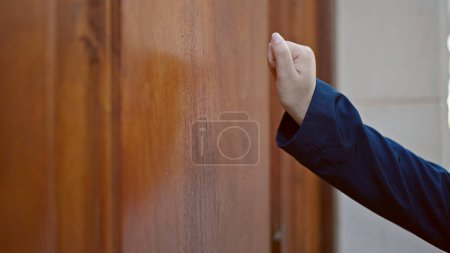 Photo for Young hispanic woman knocking at the door at street - Royalty Free Image